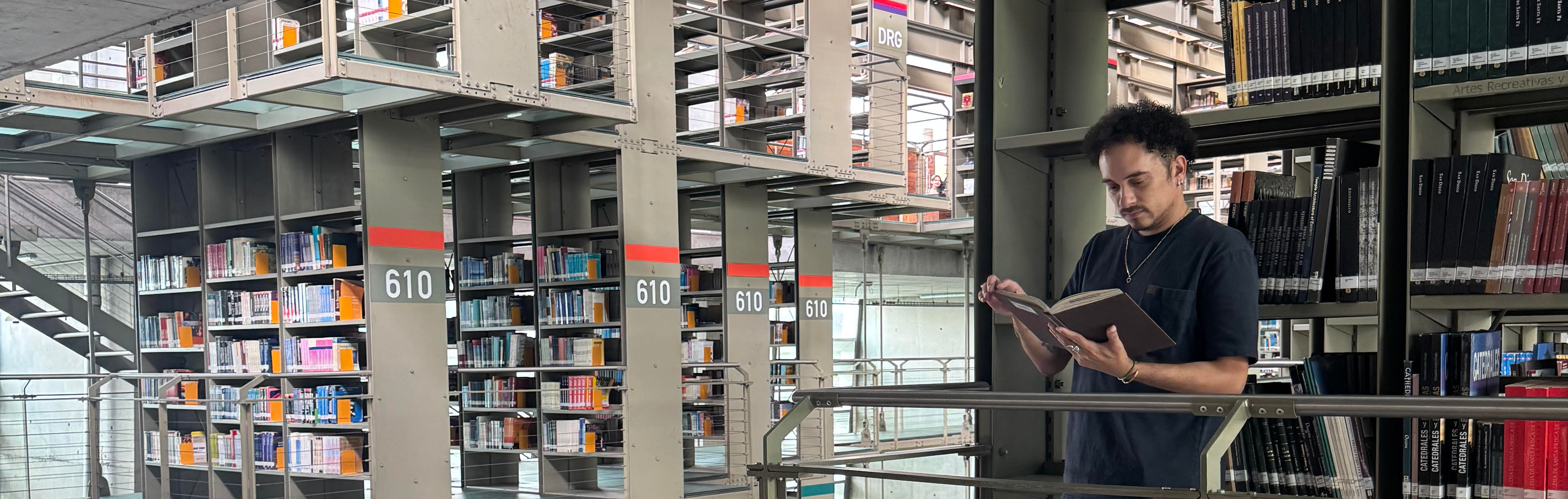 Man reading a book in a library with bookshelves in the background